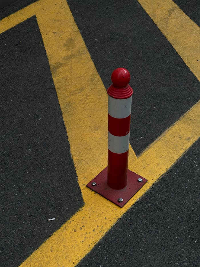 Vertical red bollard on asphalt with yellow striped lines, urban traffic safety.
